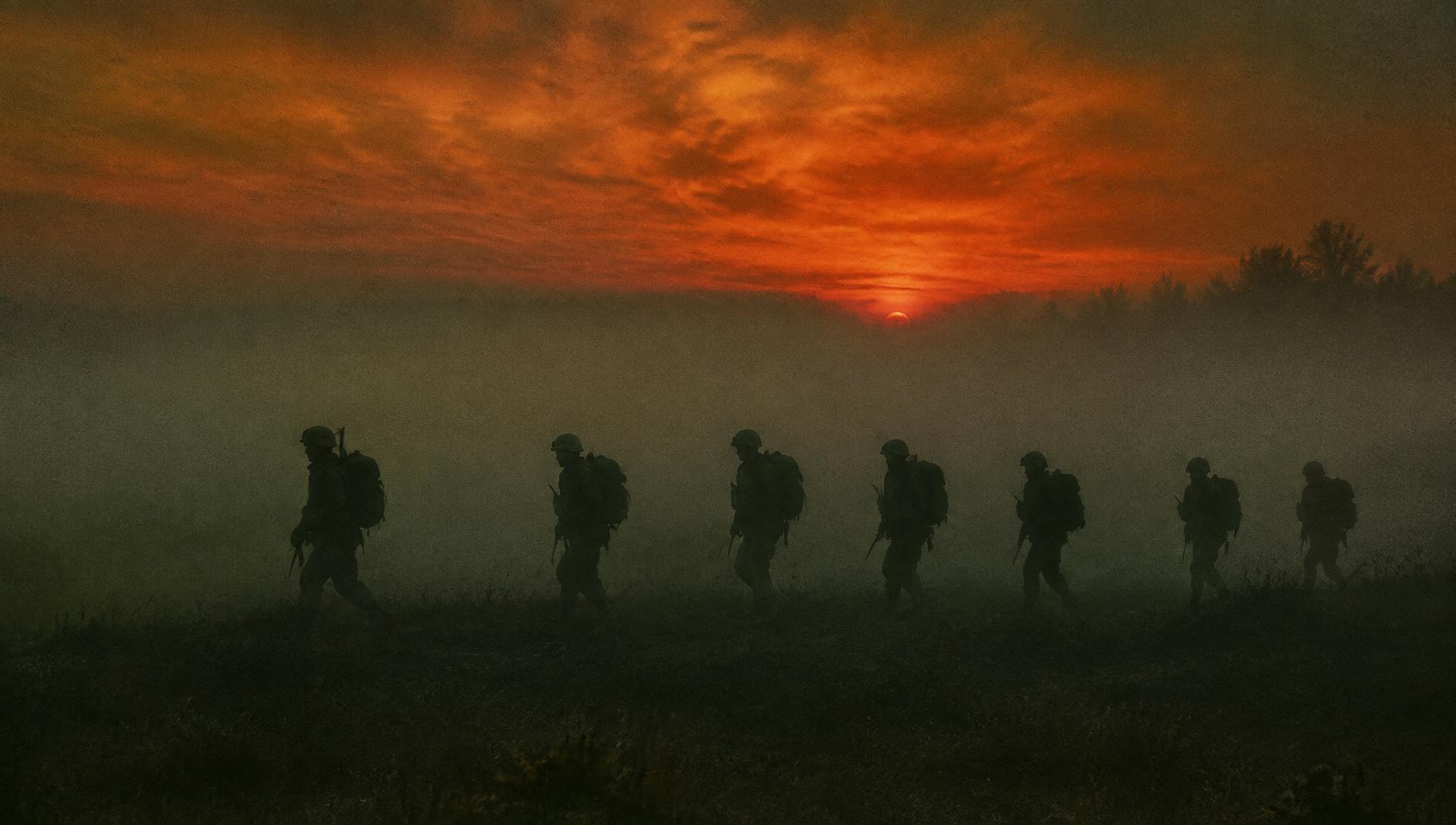 Silhouettes of soldiers marching at dawn through fog
